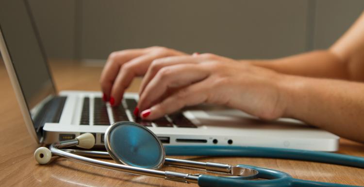 typing at a computer next to a stethoscope